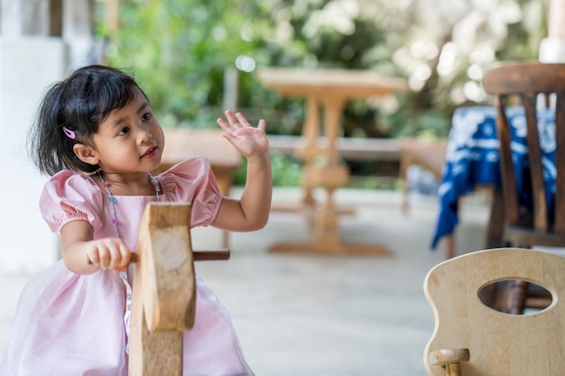 Una ragazza con un vestito rosa sta salutando un bambino su un cavallo di legno.