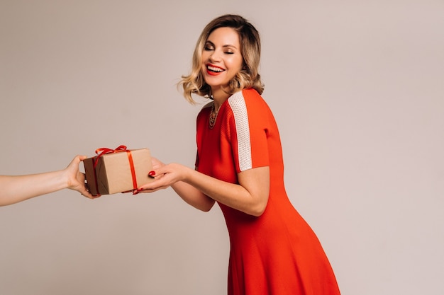 Una ragazza con un vestito rosso riceve un regalo tra le mani su un muro grigio.