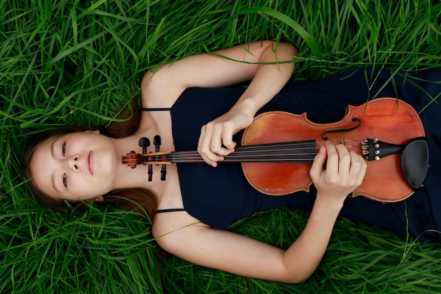 Una ragazza con un violino giace sull'erba. Aspetto asiatico. Foto di alta qualità