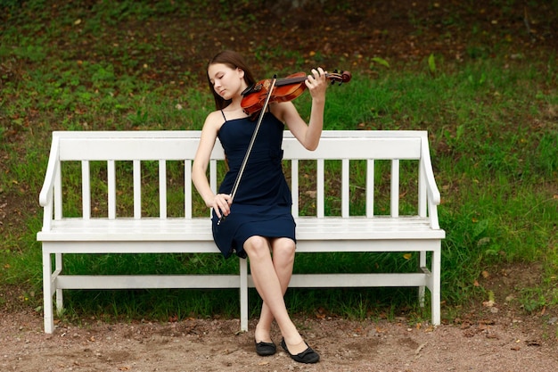 Una ragazza con un violino siede su una panchina bianca