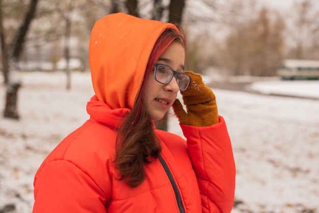 Una ragazza con una calda giacca arancione brillante. Ragazza in una giacca arancione in caso di neve. Ragazza adolescente in inverno