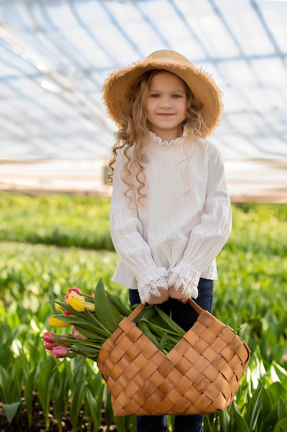 una ragazza con una camicetta bianca e un cappello di paglia tiene in mano una borsa di paglia con dei tulipani