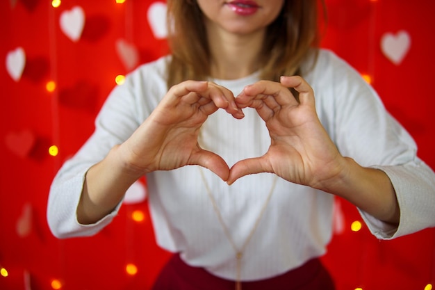 Una ragazza con una camicetta bianca mostra un cuore con le mani. Sfondo rosso. Concetto di San Valentino