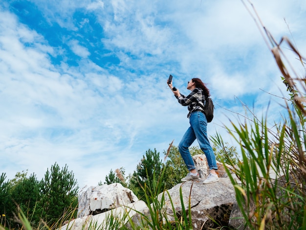 Una ragazza con una camicia a quadri cerca di catturare un telefono cellulare o una connessione Internet o si fa un selfie