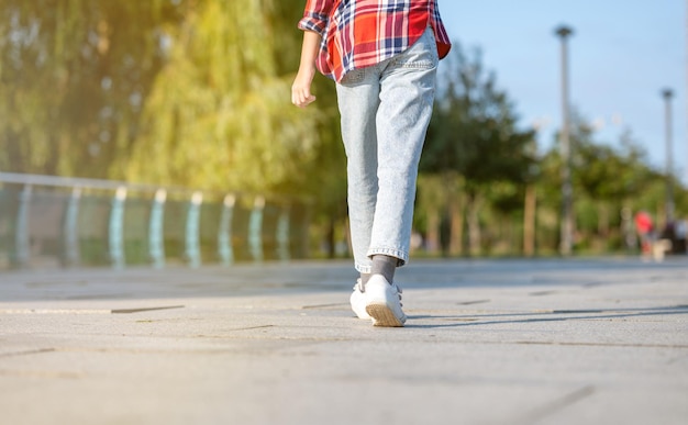 Una ragazza con una camicia a quadri salta e corre lungo un sentiero in un parco cittadino in una soleggiata giornata estiva.