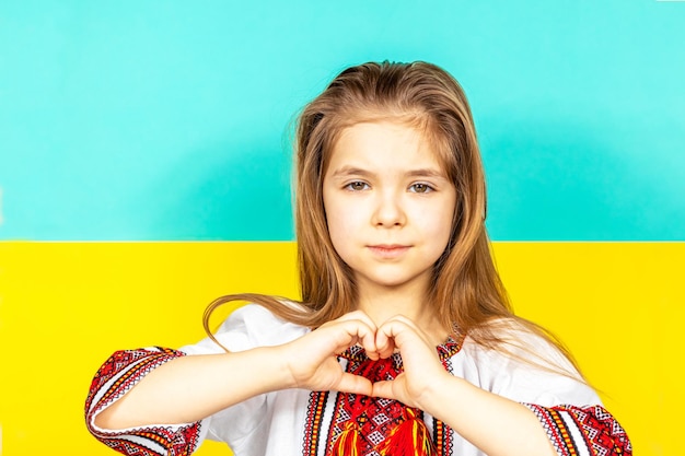 Una ragazza con una camicia ricamata mostra un segno di cuore come segno di amore per l'Ucraina in primo piano