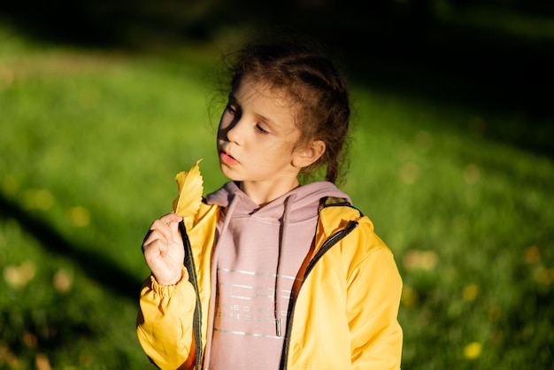 Una ragazza con una foglia gialla sotto i raggi del sole al tramonto