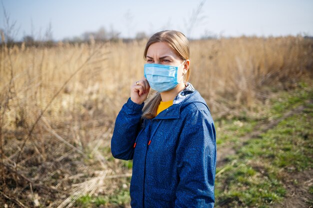 Una ragazza con una giacca blu in natura indossa una maschera medica protettiva. Maschera per la giornata di sole all'aperto sul viso dai virus