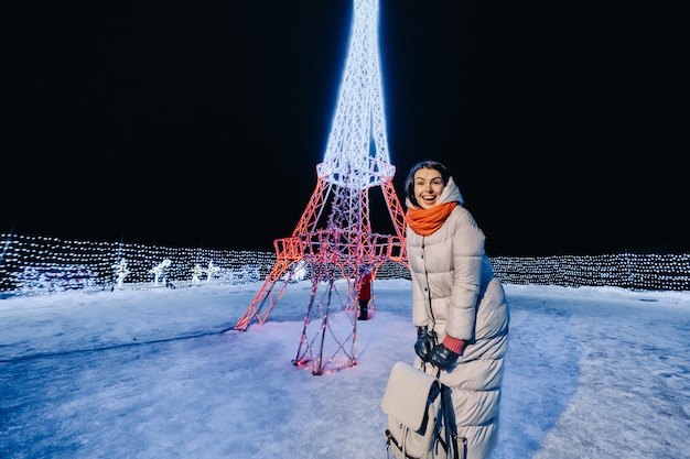 Una ragazza con una giacca grigia in inverno con le luci della sera accese sulla strada di Natale