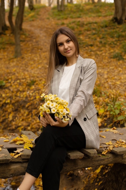 una ragazza con una giacca grigia sul ponte tiene un mazzo di fiori nella foresta autunnale urbana