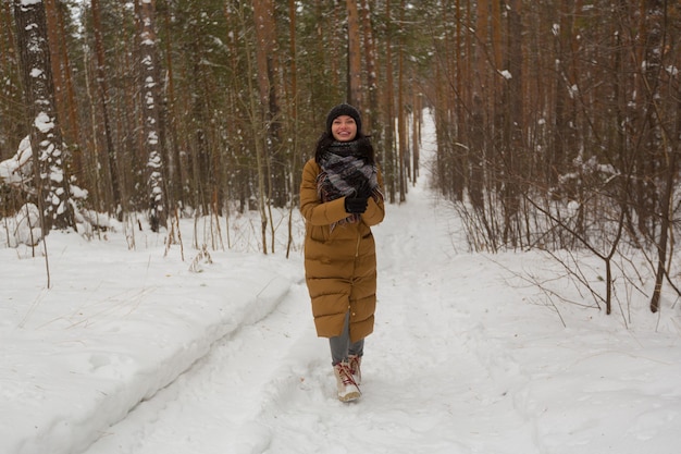 Una ragazza con una giacca marrone cammina nella foresta di neve invernale.