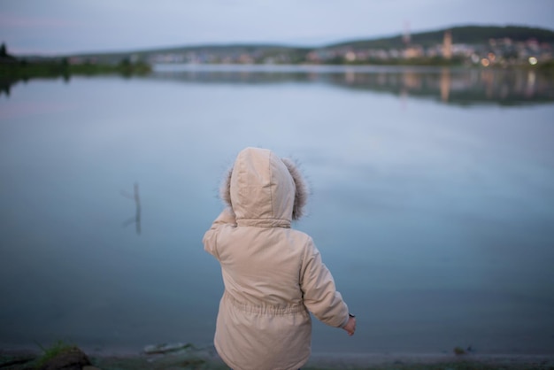 Una ragazza con una giacca sta in piedi sulla riva del fiume la sera