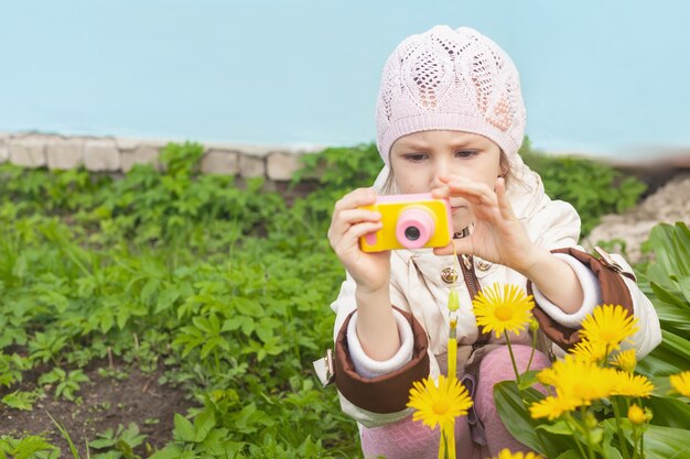 Una ragazza con una macchina fotografica gialla per bambini fotografa i fiori del giardino in primavera.