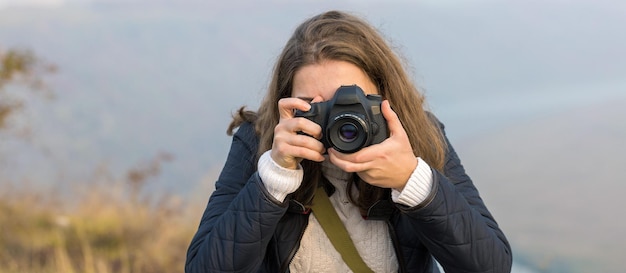 Una ragazza con una macchina fotografica in mano in una posa divertente fa una cornice Paparazi con una macchina fotografica in mano su un focolaio in montagna