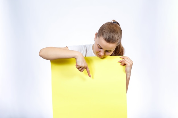 Una ragazza con una maglietta bianca tiene in mano un grande foglio di striscione bianco giallo.