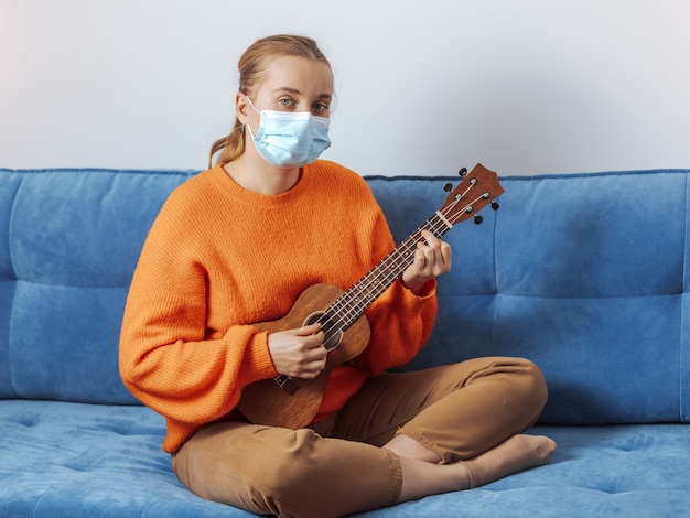 Una ragazza con una maschera medica suona l'ukulele