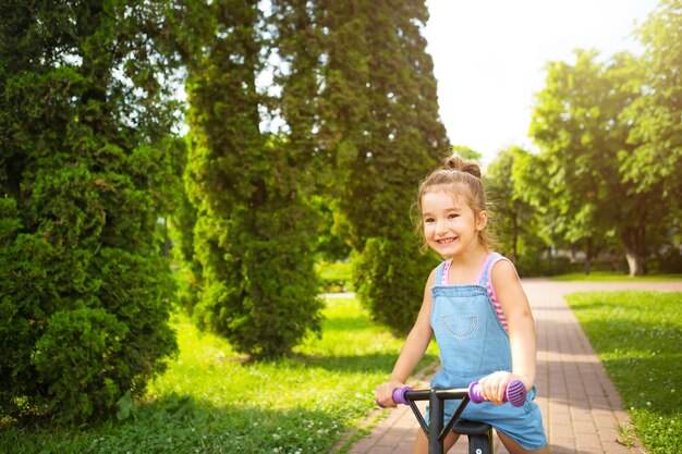 Una ragazza con una tuta di jeans guida una bici da corsa viola in estate