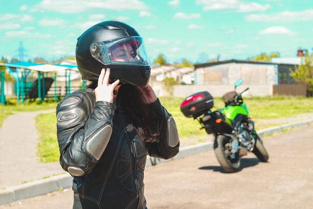 Una ragazza con una tuta protettiva in pelle da motociclista indossa un casco sullo sfondo di una motocicletta