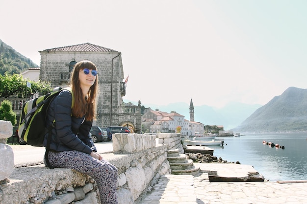 una ragazza con uno zaino si siede sull'argine della vecchia montagna e guarda il mare