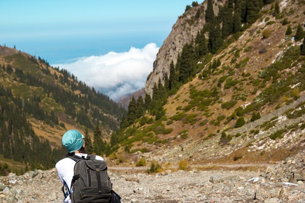 Una ragazza con uno zaino sta riposando tra le alte montagne. La gola con le nuvole.