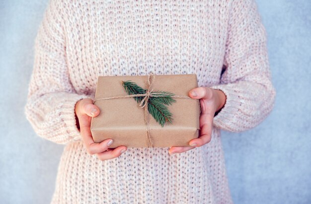 Una ragazza con zero rifiuti regalo di Natale scatola avvolta in carta kraft e decorata con abete ramo, eco friendly concetto di Natale