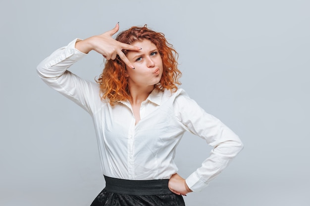 Una ragazza dai capelli rossi con una camicia bianca mostra due dita