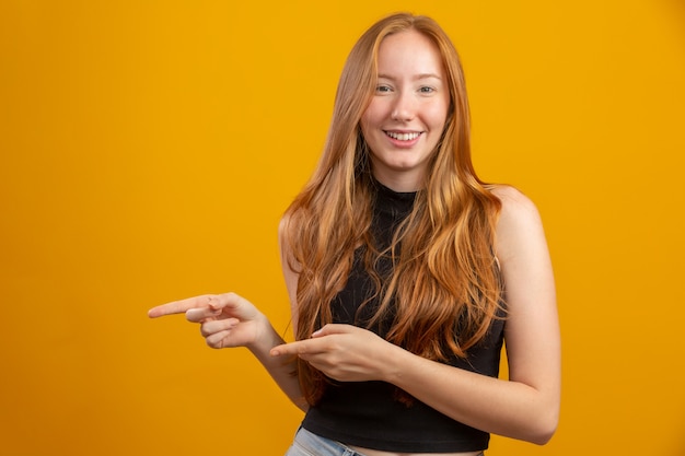 Una ragazza dai capelli rossi in giallo offre opportunità puntare il dito sul lato dello spazio libero copia per l'annuncio di contenuti promozionali.