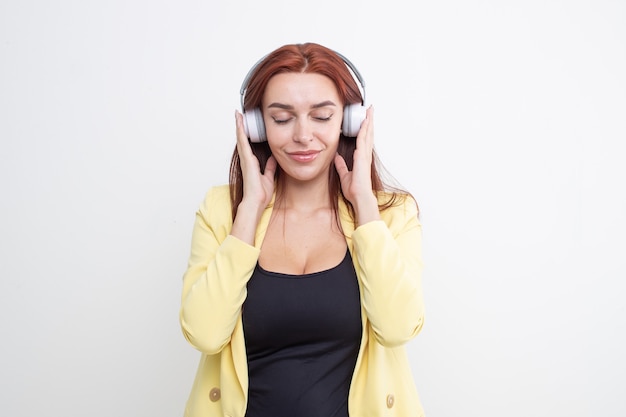 Una ragazza dai capelli rossi in un completo giallo ascolta musica in grandi cuffie