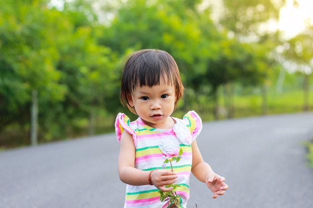 Una ragazza del bambino che sta e che tiene un'erba fiorisce in sue mani al parco naturale.