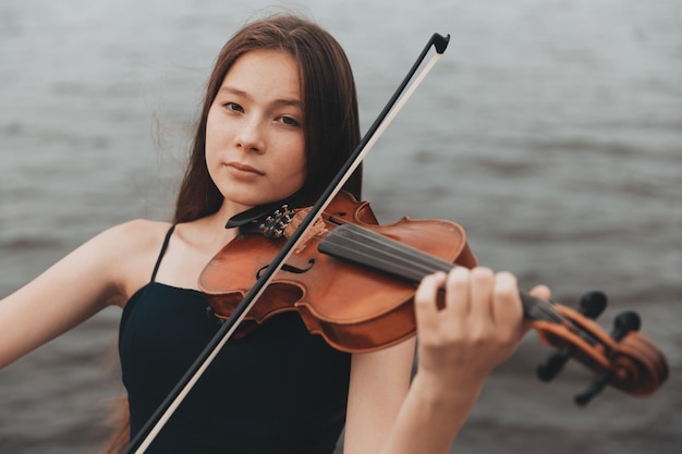 Una ragazza di aspetto asiatico suona il violino in natura. Foto di alta qualità