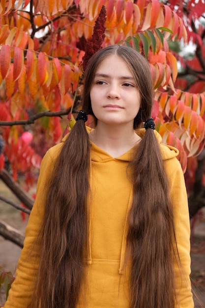 Una ragazza di un anno con i capelli lunghi con due code in una felpa con cappuccio arancione