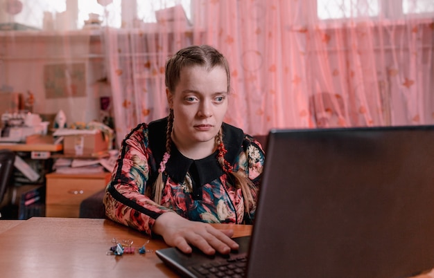 Una ragazza disabile con gli occhi a mandorla è seduta a una scrivania e lavora su un laptop. formazione per disabili