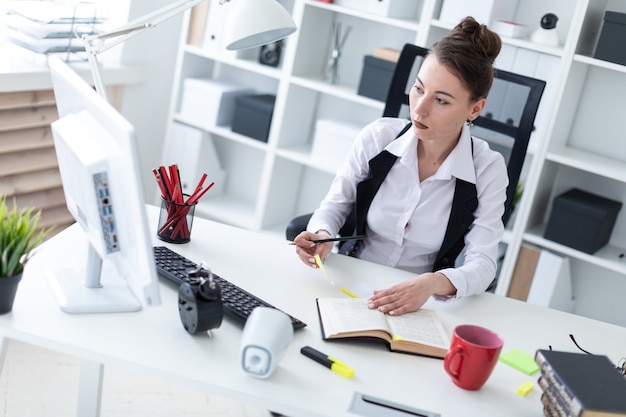 Una ragazza è seduta a un tavolo in ufficio, tiene in mano una matita e lavora con gli adesivi.