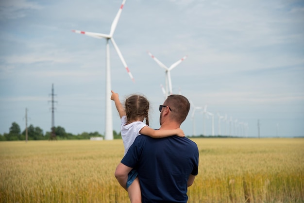 Una ragazza e suo padre guardano il generatore eolico nel campo. Ecologia. Futuro.