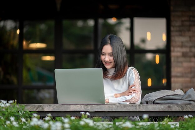 Una ragazza fa soldi online lavorando su una sedia di legno utilizzando un laptop per comunicare con i clienti tramite i concetti di trading online di Internet