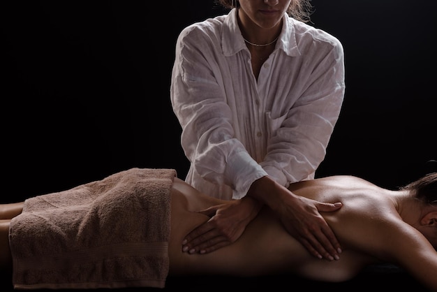 Una ragazza fa un massaggio con un primo piano di olio su uno sfondo scuro