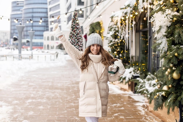 Una ragazza felice cammina per la città nella neve con un colorato lecca-lecca rotondo e una confezione regalo