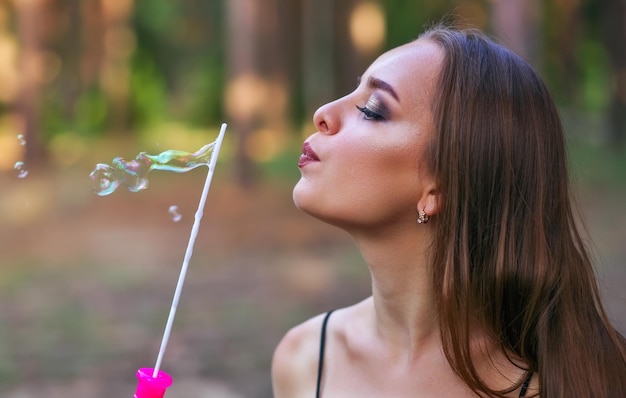 Una ragazza felice che soffia bolle di sapone nel parco estivo