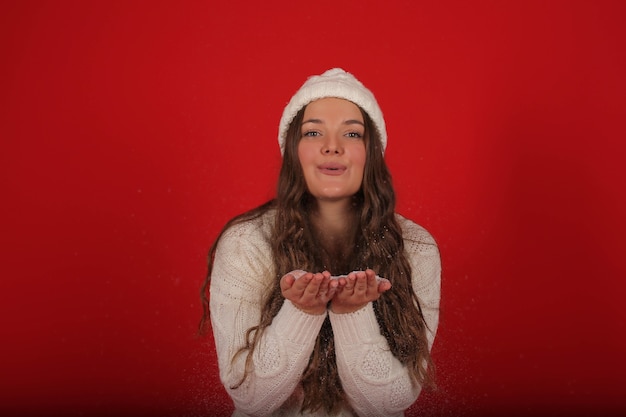 una ragazza felice con un cappello invernale e un maglione lavorato a maglia in jeans sullo sfondo della neve artificiale