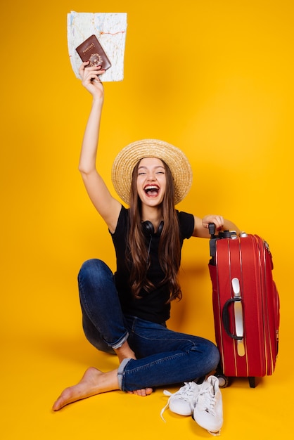 Una ragazza felice con un cappello vola in vacanza, tiene un passaporto e dei biglietti, una grande valigia con delle cose