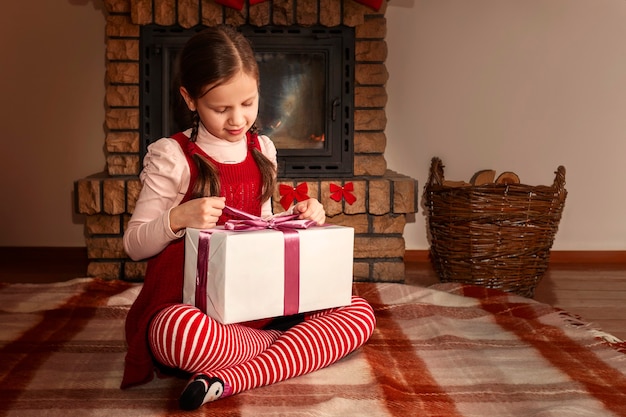 Una ragazza felice con un vestito rosso e una calzamaglia a righe scarta un regalo di Natale