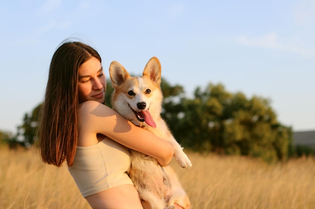 Una ragazza felice e contenta tiene in mano un simpatico cane corgi che gioca e abbraccia amorevolmente un corgi