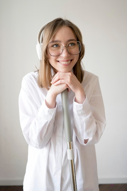 Una ragazza felice in camicia bianca con occhiali e cuffie sta pulendo la casa