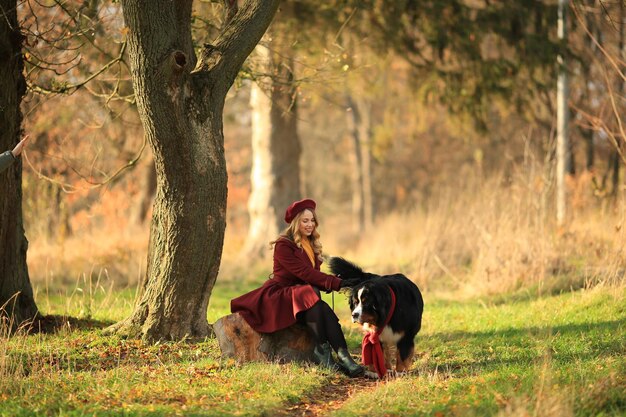 Una ragazza francese siede in un parco autunnale con il suo cane Guanti e cappotti da donna