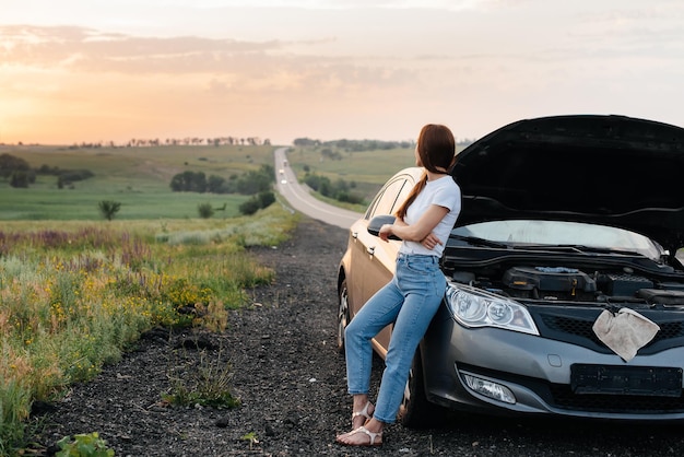 Una ragazza frustrata si trova vicino a un'auto in panne nel mezzo dell'autostrada durante il tramonto Guasto e riparazione dell'auto In attesa di aiuto Servizio auto Guasto auto su strada