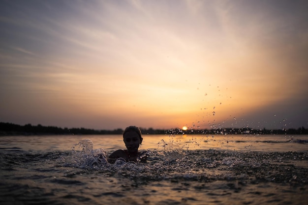 Una ragazza gioca con l'acqua nel lago e la spruzza ai lati sullo sfondo di un tramonto