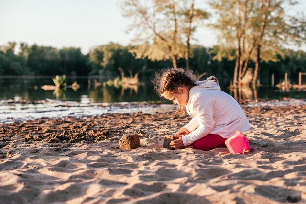 Una ragazza gioca con la sabbia su una spiaggia di sabbia sulla riva del fiume durante il tramonto.