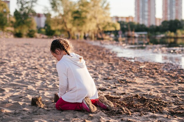 Una ragazza gioca con la sabbia su una spiaggia di sabbia sulla riva del fiume durante il tramonto.