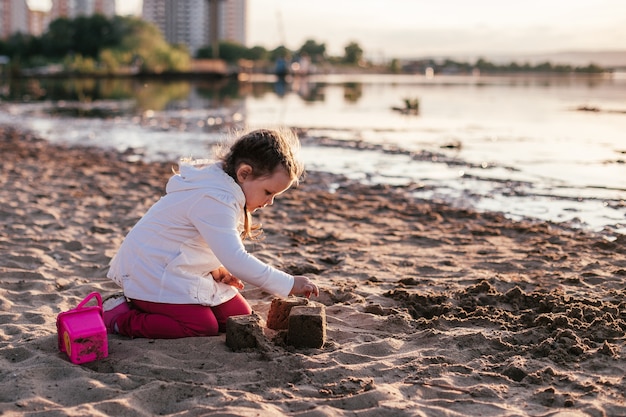 Una ragazza gioca con la sabbia su una spiaggia di sabbia sulla riva del fiume durante il tramonto.