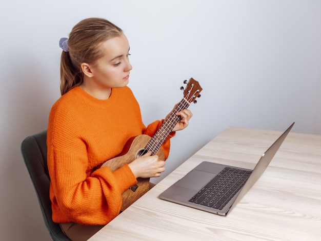 Una ragazza impara a suonare l'ukulele su un laptop